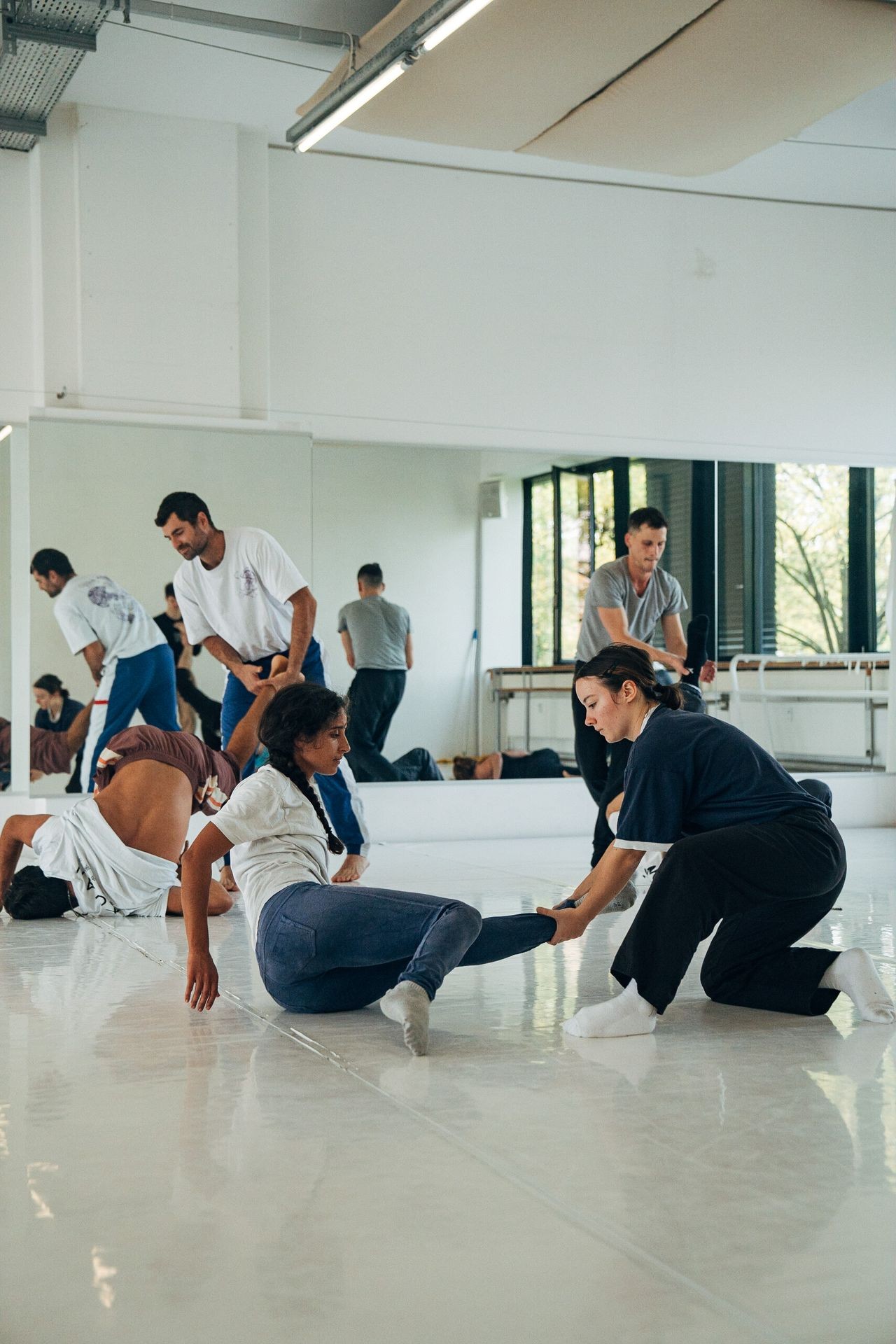 Group of people practicing dance or movement in a studio with mirrored walls and natural light.