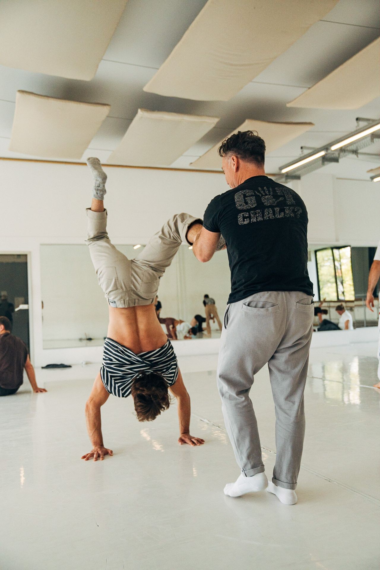 Two men practicing handstands in a dance studio with mirrored walls.