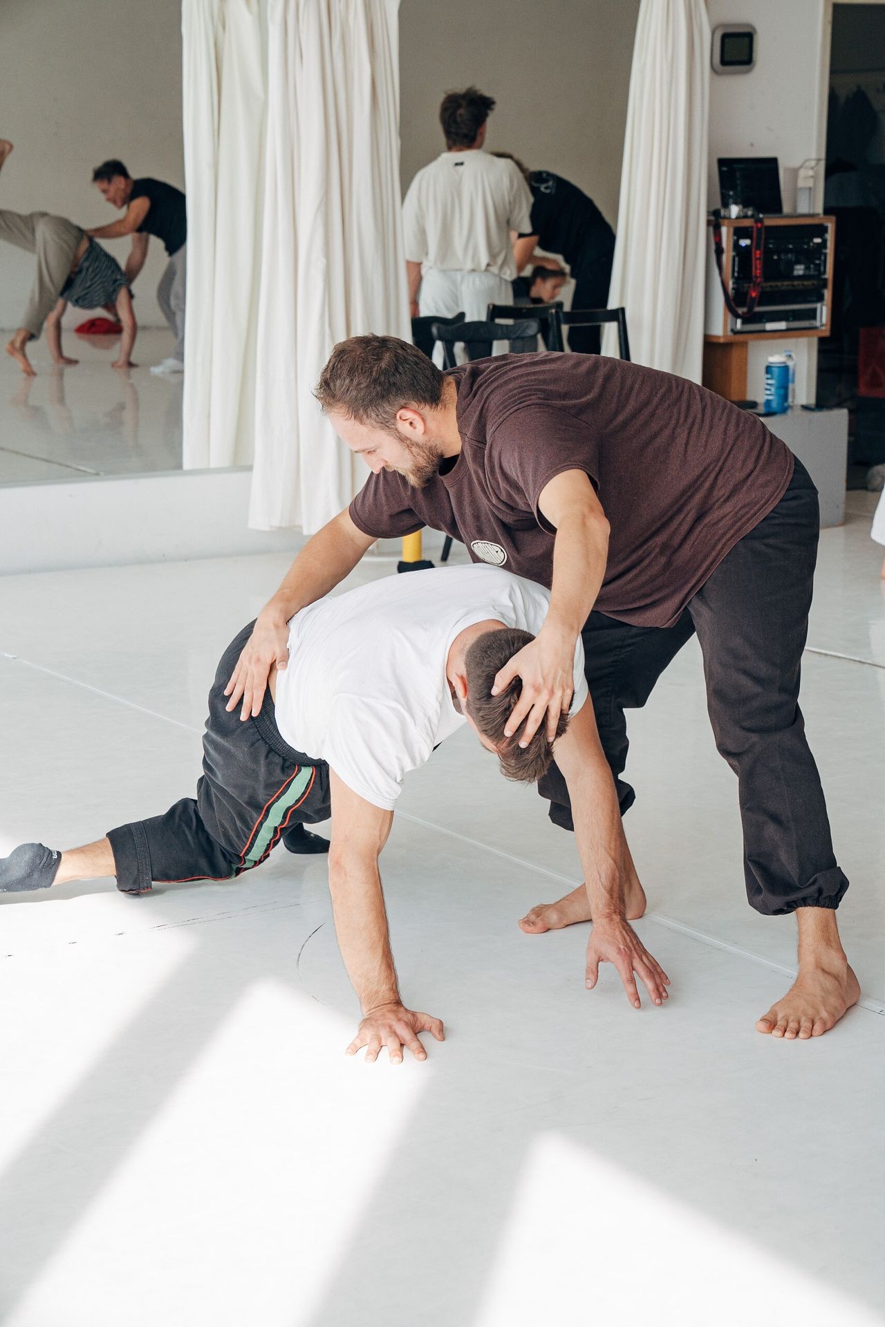 Two men practicing contemporary dance moves in a bright studio with mirrors and curtains.